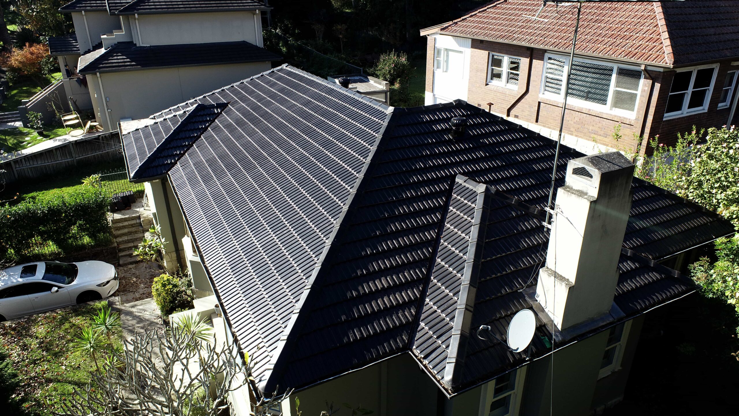 House with tiled roof solar panels, white car in driveway, neighboring homes visible. Solar panels on house roof.
