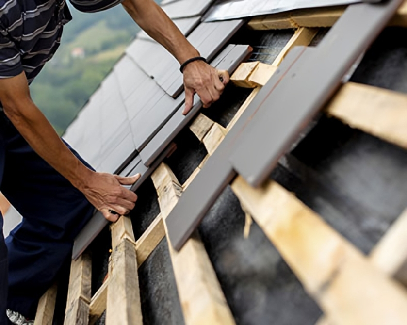 Professional asphalt shingles roof installation, person laying rectangular roof tiles on wooden framework.