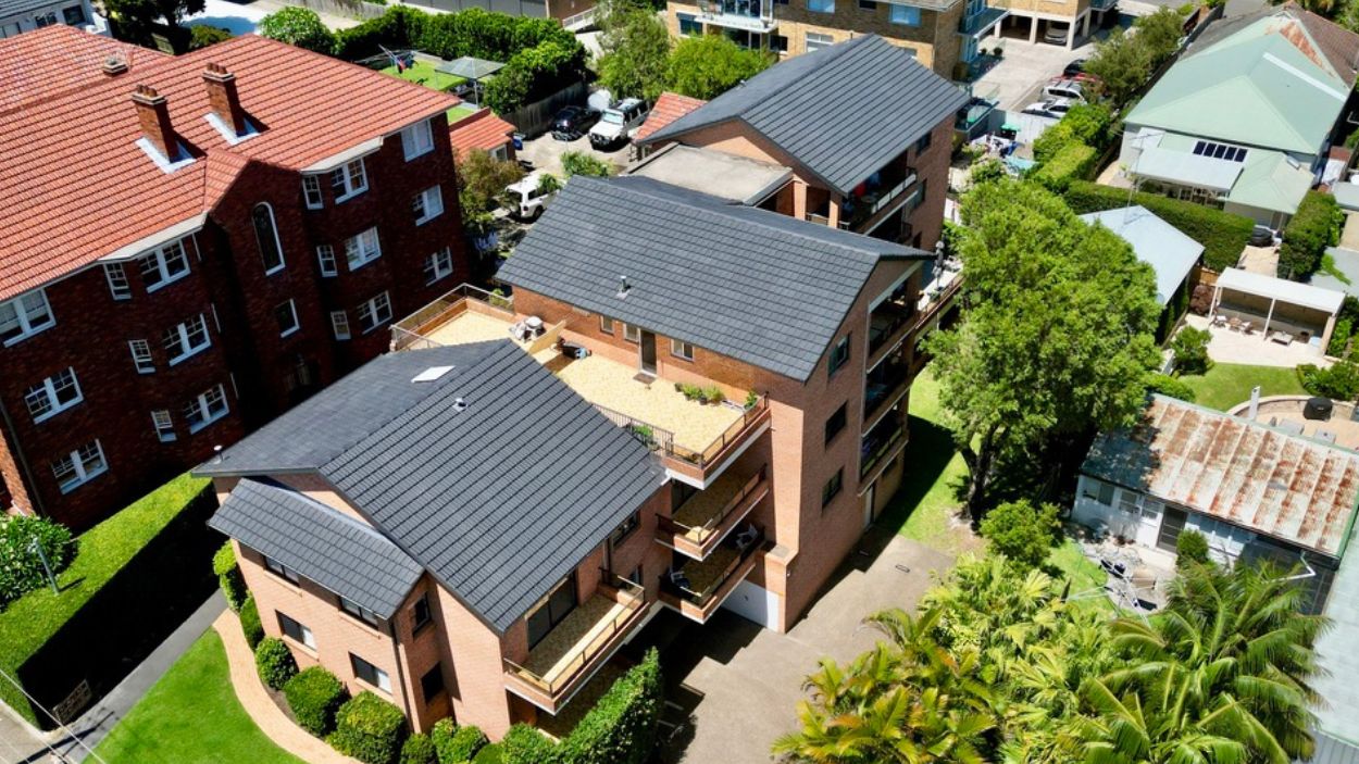 Aerial view of two brick apartment buildings with balconies, greenery, and features for longer roof lifespan.