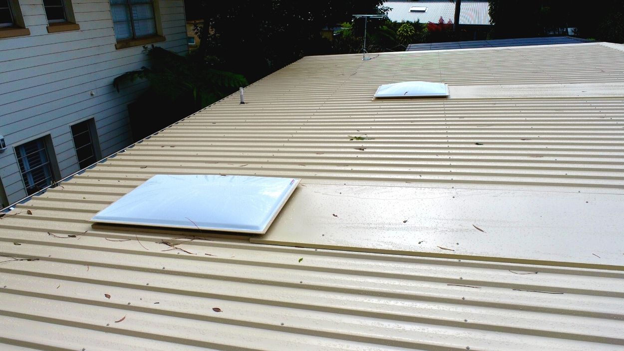 Sheet metal roof with two rectangular skylights and some debris near a white building—expert skylight installation.
